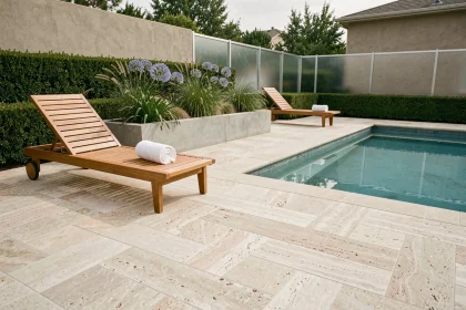Aménagement de bord de piscine moderne avec dalles en travertin, transats en teck et jardinières en béton plantées d'agapanthes
