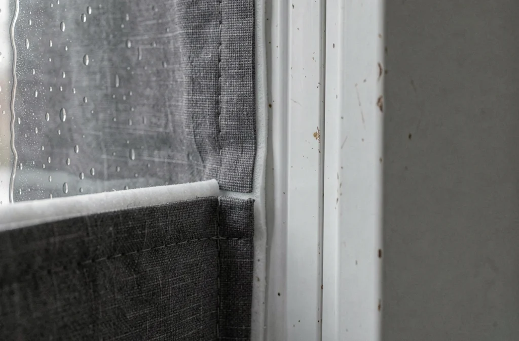 Gros plan sur la doublure isolante d'un rideau thermique devant une fenêtre avec condensation